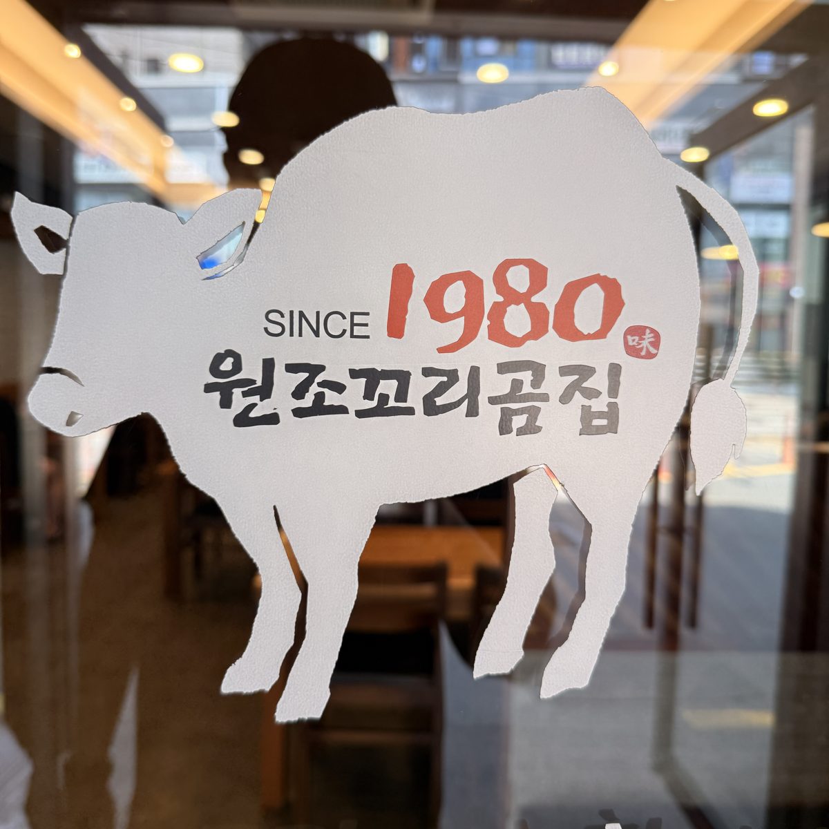 매장 유리 출입문에 붙은 소 모양 흰색 스티커. 'SINCE 1980 원조꼬리곰집'이라고 적혀 있다.